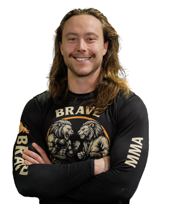 Adam Marsh with long hair, wearing a black MMA-themed shirt, standing in a fitness environment.