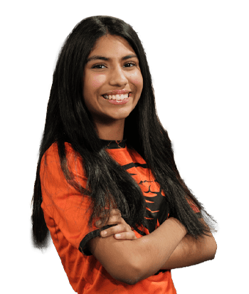 Portrait of Mia Sethi smiling confidently, wearing an orange sports jersey, with long dark hair and a friendly expression, standing against a blurred background.